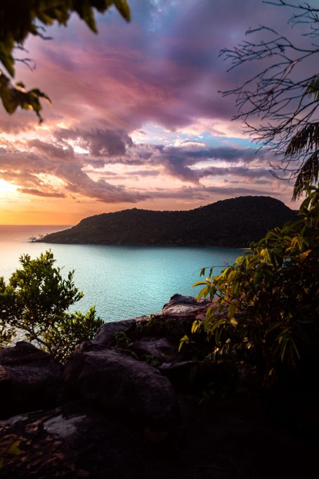 Sunset-view of a bay with turquoise water, palm trees and a dramatic sky. Paradise.